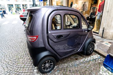 Venedik, Veneto - İtalya - 06-10-2021: Küçük mor elektrikli araba bir şehrin kaldırım taşı sokağında motosiklet park yerinde park edilmiş.