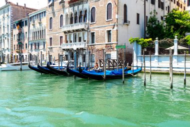 Venedik, Veneto - İtalya - 06-10-2021: Açık bir gökyüzünün altındaki tarihi Venedik binalarının yanındaki demirlemiş gondollar