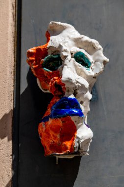 Vicenza, Venetien - İtalya - 06-12-2021: Canlı, soyut seramik yüz çizimleri turuncu ve beyaza boyanmış, yeşil gözlü ve mavi ağızlı, Vicenza 'da bir duvara monte edilmiş.