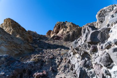 Cabo de Gata, Almeria - İspanya - 01-23-2024: Açık bir gökyüzü altında katmanlı kayaları olan Stark volkanik manzarası