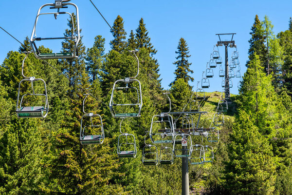 Obertauern, Salzburg - Austria - 06-16-2021: A Chairlift with empty chairs ride through lush greenery on a clear day in the Austrian mountains, inviting summer explorers