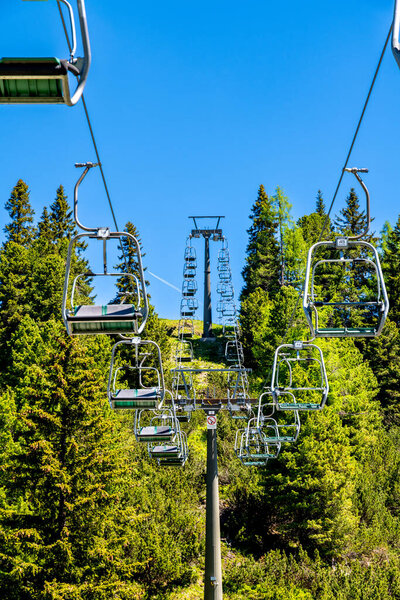 Obertauern, Salzburg - Austria - 06-16-2021: A Chairlift with empty chairs ride through lush greenery on a clear day in the Austrian mountains, inviting summer explorers