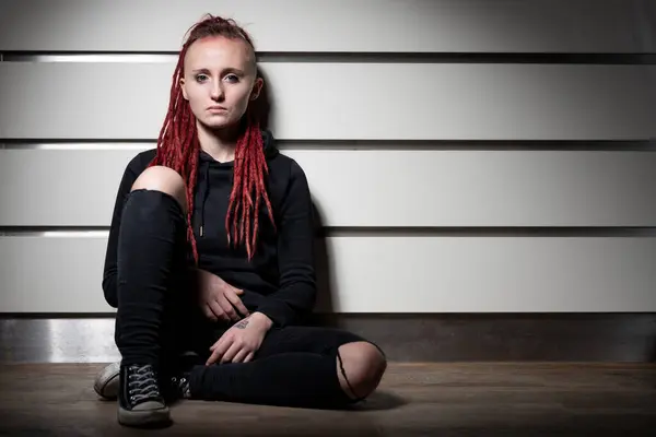 Çizgili bir duvara yaslanmış siyah elbiseli ve rastalı kadın.