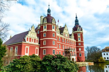 Bad Muskau, Saksonya - Almanya - 04-18-2021: Iconic Schloss Muskau, Muskau Parkı 'nda, yapraksız bir ağaç ve Fuerst Pueckler parkında yemyeşil bir göletin arkasında yuva yapmış.
