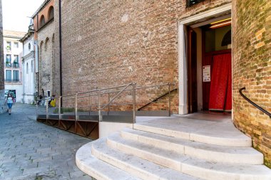 Treviso, Venetien - İtalya - 06-08-2021: Bir metal tekerlekli sandalye rampası ve havari Aziz Peter Katedrali 'nin yan girişinde akan kırmızı bir kumaşa giden beyaz eğimli adımlar
