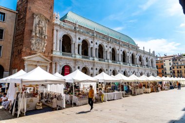 Vicenza, Venetien - İtalya - 06-12-2021: Basilica Palladiana, Vicenza, İtalya 'nın tarihi sütununun tarihi zeminine karşı beyaz katlanmış bir sıra beyaz pavyonla çeşitli ve canlı bir pazar