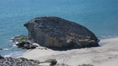 Akdeniz 'deki bir plajda büyük bir kayanın görüntüsü, onu gün ışığında ıssız plajın üzerinde bir tepsi takip ediyor.