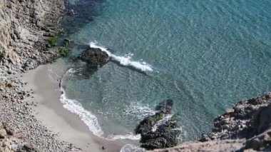 Yukarıdan, dalgaların iki küçük kaya tarafından ayrılıp kırıldığı ve suyun sahile doğru köpürdüğü küçük bir koya bakın..