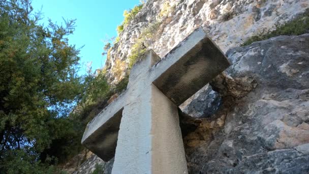 崖の壁に立っている大きな石の十字架の景色は 下から撮影され 崖の壁と十字架が上昇します 頂上には青い空が見える — ストック動画
