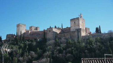 Alhambra 'yı Granada, İspanya' nın dışından, sağdan sola, parlak mavi bir gökyüzünün altından süpür. Ön planda, eski moda bir anten görülebilir.