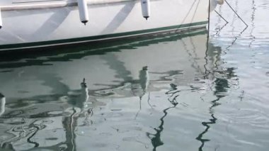 İki çamurluğu olan bir geminin alt kısmı, liman havzasının suyuna yansıyan, yumuşak dalgalar ve parlak gün ışığıyla..