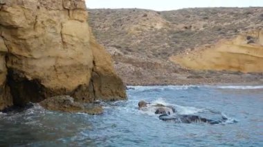 Kayalık kıyı şeridinden bir körfez boyunca uzanan kaya yarıkları ile mavi gökyüzünün altında ince bulutlarla birlikte..