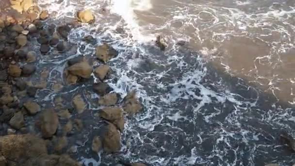 岩の海岸線に衝突する海の波は 海に戻る方法を見つけるために多くの泡と渦を生み出します 水は非常に乱れています — ストック動画