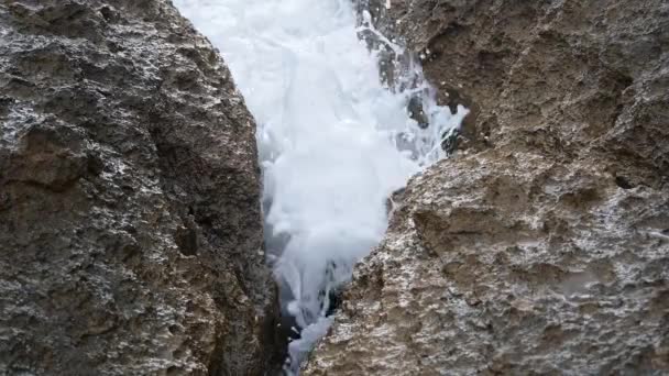一种岩石裂缝 中间有一个小岩石 海水被波浪反复冲刷 形成一条穿过泡沫水面的小路 — 图库视频影像