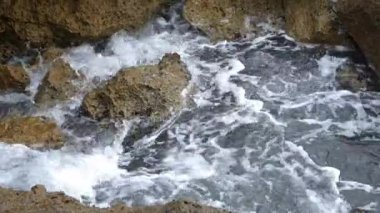 Su, kayalar ve taşlar boyunca akıyor ve sıçrıyor. Ardından bir kamera tepsisi açık denize doğru ilerliyor. Suyun kabardığı yerden.