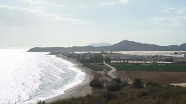 Güneş ışığının arkasındaki kıyı şeridi boyunca yukarıdan bak. Dalgaların kıyıya vurduğunu ve sahil boyunca kıvrılan bir yol görülebiliyor..