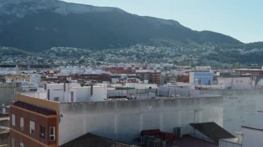 Denia, Alicante - İspanya 11-04-2023: Denia şehri üzerinde çanlar, çok katlı binalar, çatı bahçeleri ve mavi gökyüzünün altında dağlarla süpür..