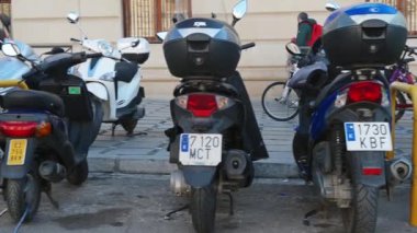 Granada, Granada - İspanya 02-03-2024: Belirlenmiş park alanlarında sıralanmış ve raflara sabitlenmiş çeşitli büyüklükteki scooterlar ve motorsikletler üzerinden sağdan sola yavaş tava