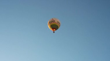 Guadix, Granada - İspanya 01-25-2024: Sabah güneşinin aydınlattığı reklamlarla dolu sıcak hava balonu mavi, bulutsuz gökyüzüne yükseliyor ve uzaklaşıyor.