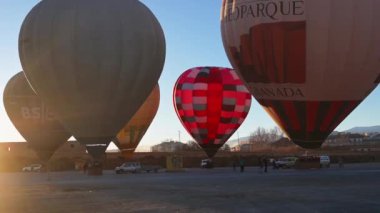 Guadix, Granada - İspanya 01-25-2024: Kalkıştan kısa bir süre önce sabah güneşi tarafından aydınlatılan, pek çok dik sıcak hava balonunun sabah rüzgarında sallandığı büyük bir meydanın üzerinde kamera yansıması.