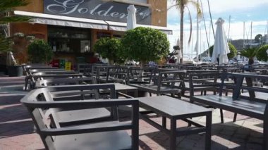 Mazarron, Murcia - İspanya 03-26-2024: Altın Kafe restoranının sayısız boş sıraları ve masaları üzerinde bir tava. Hiçbir misafir görünmüyor ve şemsiyeler kapalı kalıyor..
