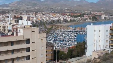 Mazarron, Murcia - İspanya 03-26-2024: Marinanın, yüksek binaların ve şehrin üzerinden soldan sağa doğru bir pan, Puerto de Mazarron 'un suyuna geri dönüyor.
