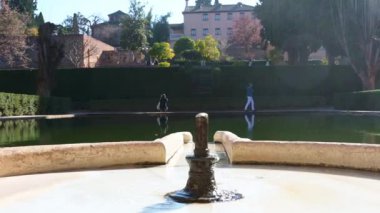Granada, Granada - İspanya 01-27-2024: Alhambra 'nın avlusundaki bir su havzasına kaynayan bir fıskiyenin üzerinden bakın. Havzanın sonunda ziyaretçiler taşınıyor.