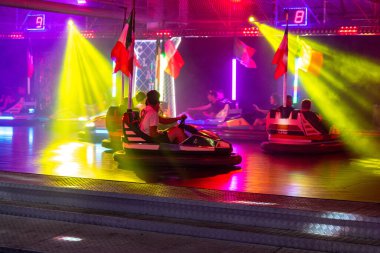 Angera, Lombardei - İtalya - 07-02-2024: Ziyaretçiler canlı ışıklar altında giderken bayraklı renkli çarpışan arabalar.