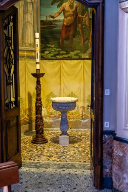 Brunate, Lombardei - Italy - 06-28-2024: A baptismal font in a chapel with murals, symbolizing the Christian baptism. clipart