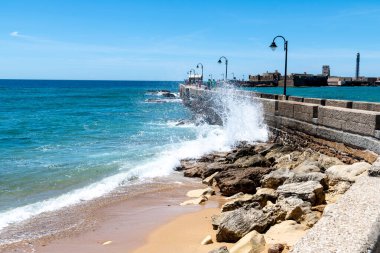 Cadiz, Cadiz - İspanya - 05-06-2024: Dalgalar Cadiz 'deki iskele duvarına çarpıyor, parlak bir gökyüzü altında, engin mavi deniz ve ufuk manzaralı.