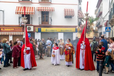 Castro del Rio, Cordoba - İspanya - 03-24-2024: Semana Santa döneminde kalabalık bir sokakta kırmızı ve beyaz cüppeli kapüşonlu katılımcıların yer aldığı bir Paskalya alayı.