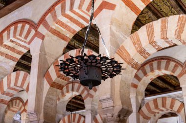 Cordoba, Cordoba - İspanya - 04-08-2024: Mezquita-Katedral de Cordoba içindeki kırmızı ve beyaz kemerler, İslami ve Hıristiyan unsurları harmanlayan dekoratif bir avizeyle eşleştiriliyor..