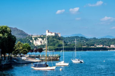 Arona, Piemont - Italy - 07-04-2024: View of Rocca di Angera fortress overlooking Lake Maggiore, with several sailboats in the foreground. clipart