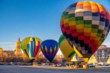 Guadix, Granada - İspanya - 01-24-2024: Mavi, sarı ve kırmızılı birkaç balon fırlatılmaya hazır. Arka planda binalar ve açık gökyüzünün altında bir kilise kulesi var..