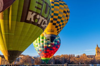 Guadix, Granada - İspanya - 01-24-2024: Birkaç renkli sıcak hava balonu, yeşil bir KITCHEN balonu ve kareli sarı-mavi bir balonun yer aldığı fırlatmaya hazır.