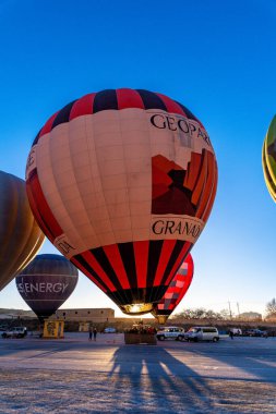 Guadix, Granada - Spain - 01-24-2024: A large red and black hot air balloon labeled GRANADA and GEOPARK is being prepared for launch against a warm sunset background. clipart