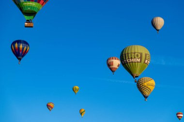 Guadix, Granada - İspanya - 01-24-2024: Birkaç renkli sıcak hava balonu açık mavi gökyüzüne yükseliyor. Büyük yeşil bir Eurokitchen balonu sağ tarafa hükmediyor ve canlı bir sahne oluşturuyor..