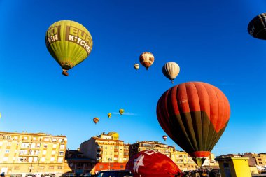 Guadix, Granada - İspanya - 01-24-2024: Bir şehrin üzerindeki açık mavi gökyüzünde birkaç sıcak hava balonu yükseliyor. Kırmızı bir balon ön planda, yeşil bir balon ise baskın..