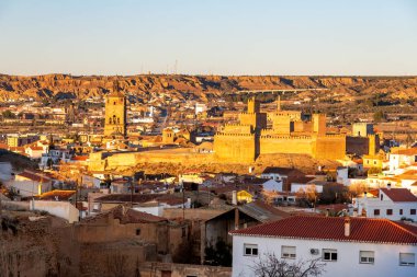 Guadix, Granada - Spain - 01-24-2024: A close-up of the Alcazaba of Guadix, a medieval Moorish fortress illuminated by the evening sun, surrounded by cave houses and modern buildings. clipart