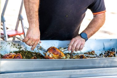 Guadix, Granada - Spain - 01-24-2024: A vendor cuts grilled chicken in a stainless steel bowl, surrounded by herbs and spices, with a watch on his wrist. clipart