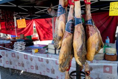 Guadix, Granada - İspanya - 01-24-2024: Bir market tezgahında asılı çok sayıda İber jambonu, arka planda orijini ve fiyatını gösteren işaretler, ahırı kaplayan kırmızı bir kumaş.