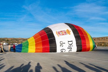 Guadix, Granada - İspanya - 01-24-2024: Otoparkta Diputacion de Granada logosu bulunan sıcak hava balonu zarfı, açık mavi gökyüzü altında yarı şişmiş, gölgelerle çevrili.