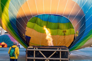 Guadix, Granada - İspanya - 01-24-2024: Zarfın altında alevler olan büyük bir sıcak hava balonu. Önünde sarı ceketli bir adam duruyor, balon yavaşça doluyor..