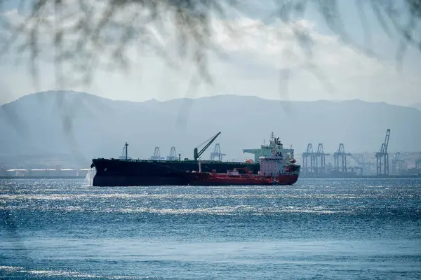 Cebelitarık açıklarındaki açık denizde geniş bir kargo gemisi arka planda vinçler ve dağlarla demirlemiş..