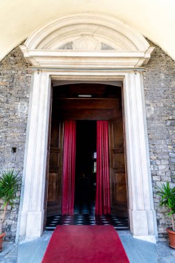 Gravedona, Lombardei - Italy - 06-24-2024: The entrance of Chiesa di San Vincenzo showcases a red carpet, flanked by stone walls and adorned with red curtains. clipart