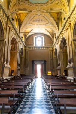 Gravedona, Lombardei - İtalya - 06-24-2024: Chiesa di San Vincenzo 'nun iç kesimi, uzun, süslü duvarlar ve büyük bir vitraylı pencereyle çevrili bir haç ve sunağı ön plana çıkarıyor.