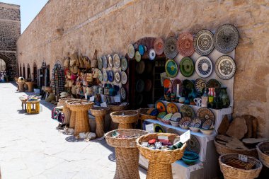 Essaouira, Marrakesch-Safi - Fas - 07-27-2024: Essaouira 'da renkli seramik kaplar ve kumtaşı duvar boyunca örülmüş sepetlerle geleneksel pazar.