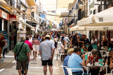 Ronda, Malaga - İspanya - 06-04-2024: İspanya 'nın Ronda kentinde yaz atmosferinin keyfini çıkaran yayalar ve kafe ziyaretçileriyle dolu hareketli bir alışveriş caddesi.