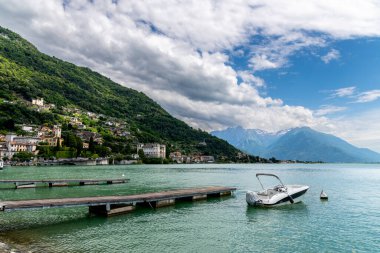 Como Gölü üzerinde geniş bir manzara ön planda çeşitli rıhtımlar, dağlar ve kısmen bulutlarla kaplı yeşil tepeler gösteriyor..