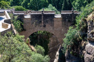 İspanya 'nın Ronda kentinde bulunan tarihi bir taş köprü olan Puente Viejo, yemyeşil ve ağaçlarla çevrili bir vadiyi kaplar..